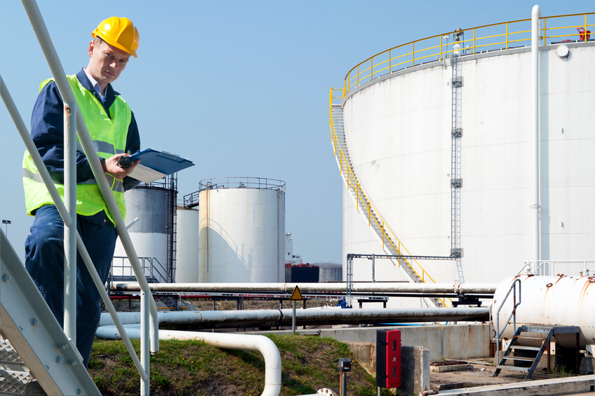 Engineer with a clipboard taking notes of the quality and state of oil silos of a petrochemical industry for safety reasons